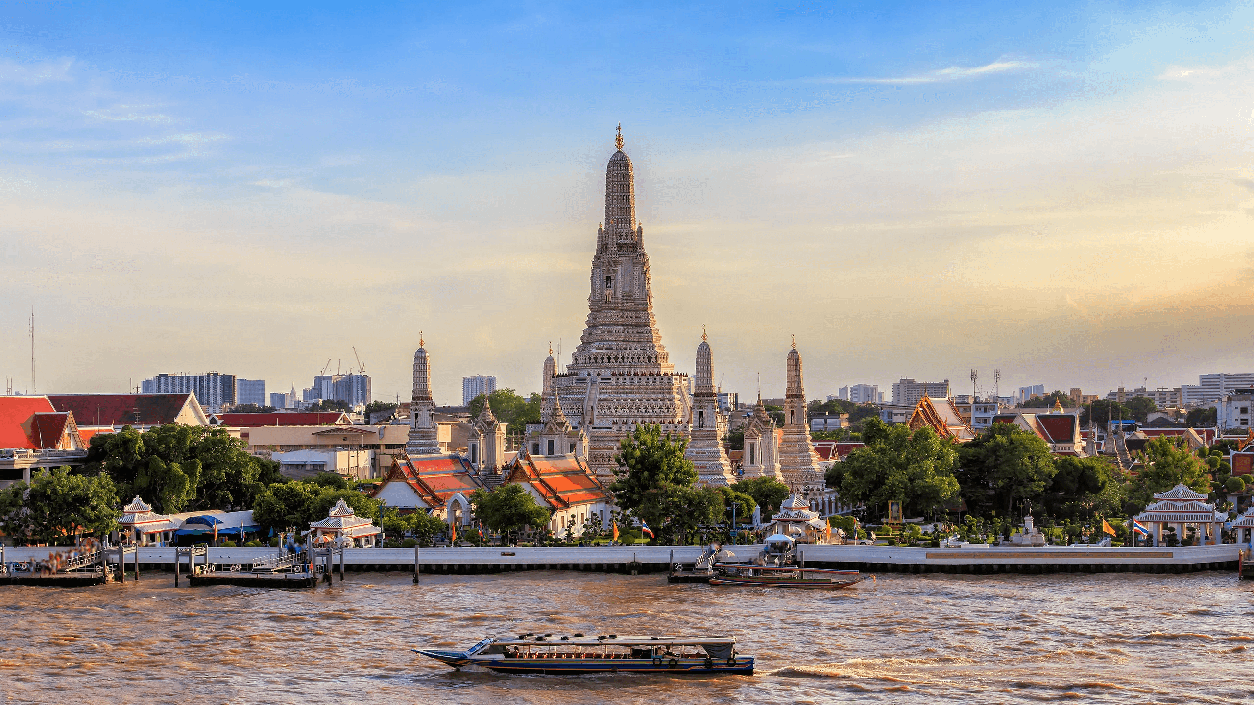 Le grand prang de Wat Arun et ses prangs d’angle vus depuis le fleuve en fin de journée, une embarcation au premier plan.